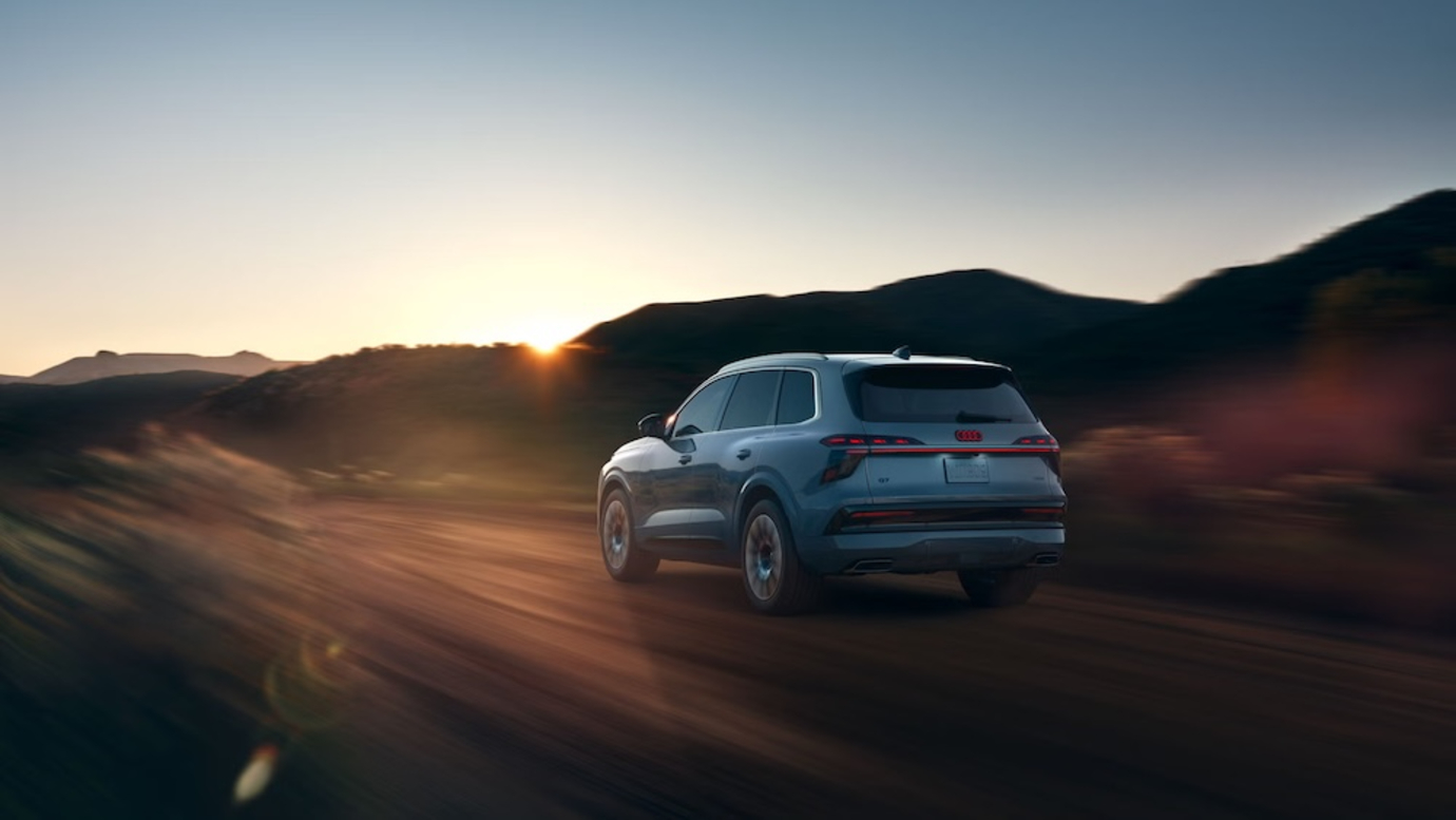 A gray-blue 2027 Audi Q7 SUV driving down a dirt road