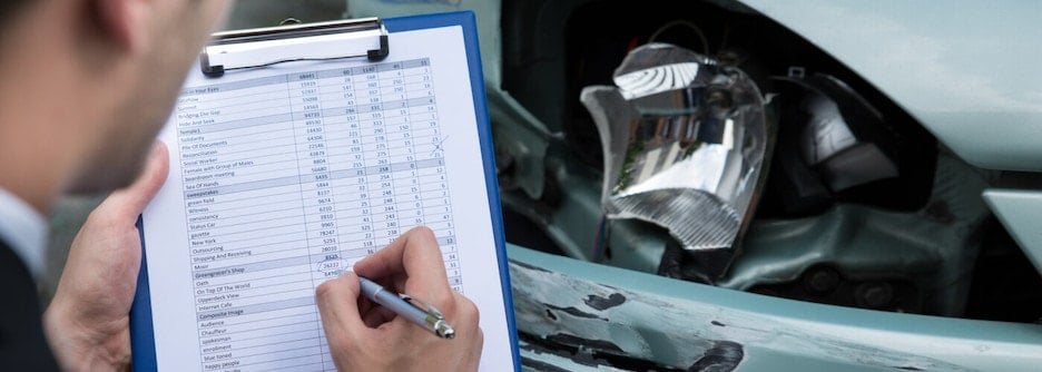 A man filling out a form looking at a damaged car.