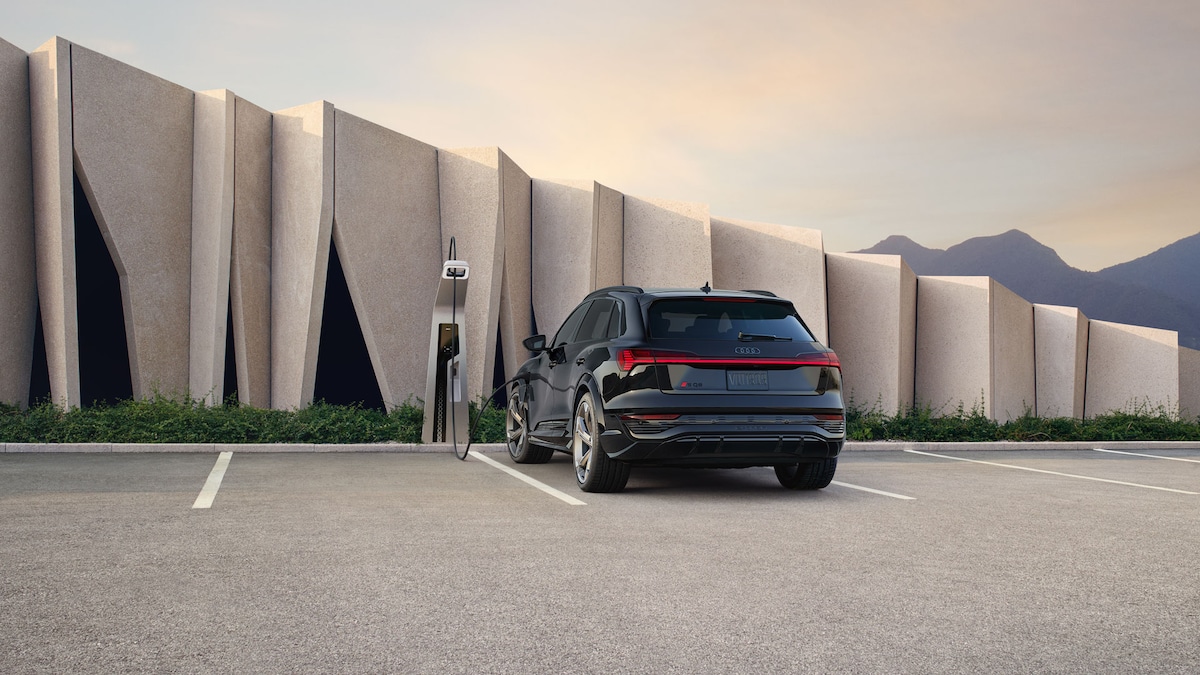Back view of a black 2024 Audi SQ8 e-tron plugged into a charger