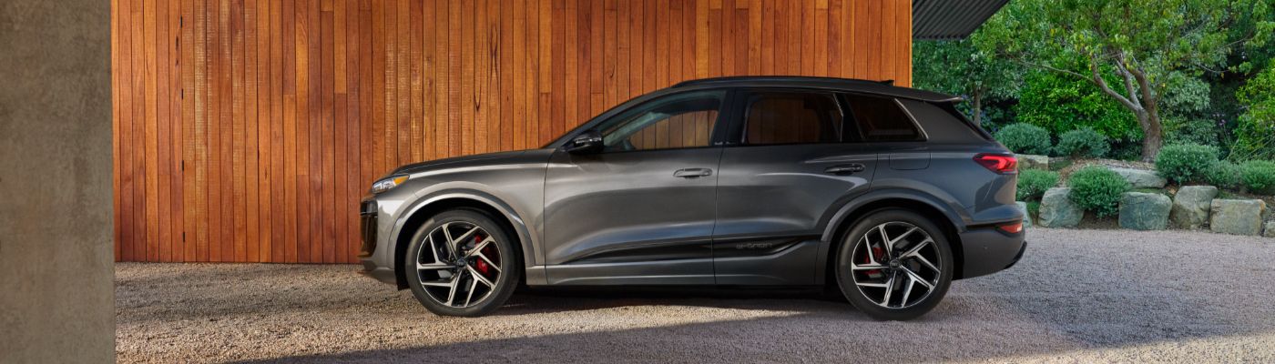 Gray Audi SQ6 e-tron parked in front of a cedar wooden structure near a green garden