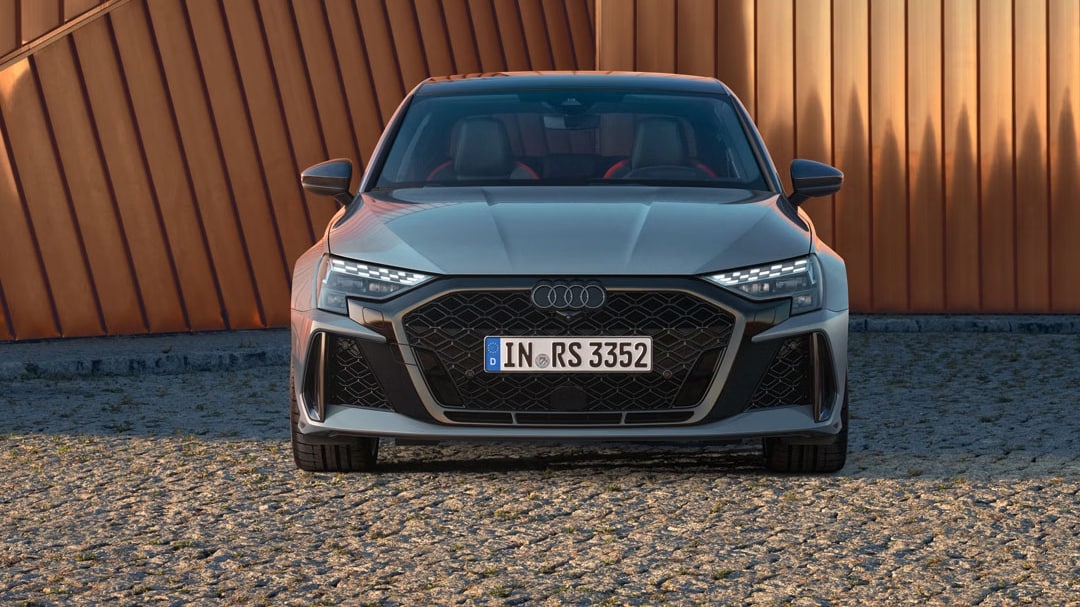 Vue avant de l'Audi RS 3 2025 garé devant un batîment, avec coucher de soleil