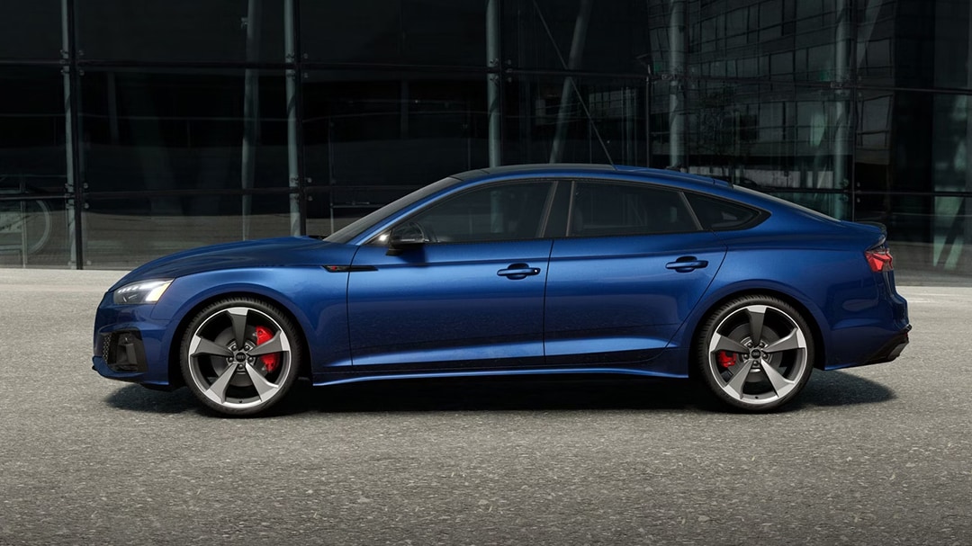 Vue latérale de l'Audi A5 Sportback 2025 garé devant un batîment avec phares allumées