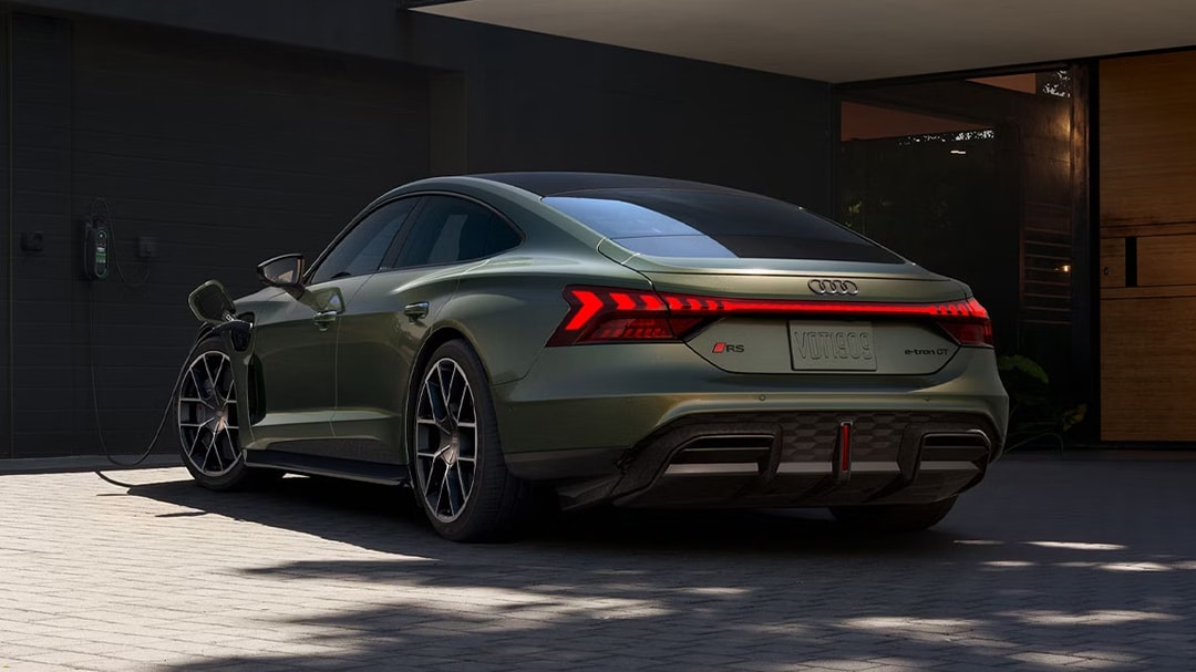 Rear view of the Audi RS e-tron GT 2025 charging in front of a house
