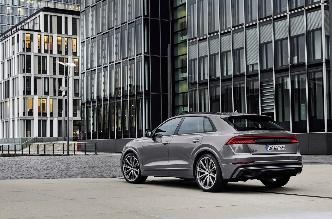 Vue 3/4 arrière d'un VUS Audi Q8 gris garé à côté d'un gratte-ciel