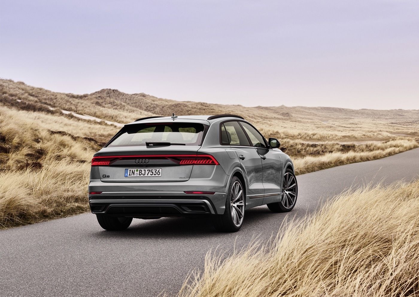 Vue 3/4 arrière d'un VUS Audi Q8 2022 gris garé sur un chemin au bord d'un champs de foins