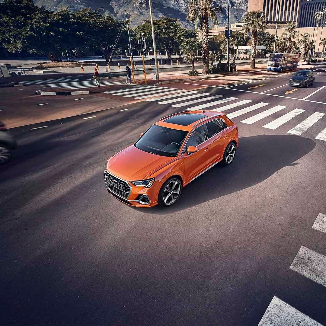 Vue de dessus d'un VUS Audi Q3 de couleur orange roulant sur un boulevard en ville