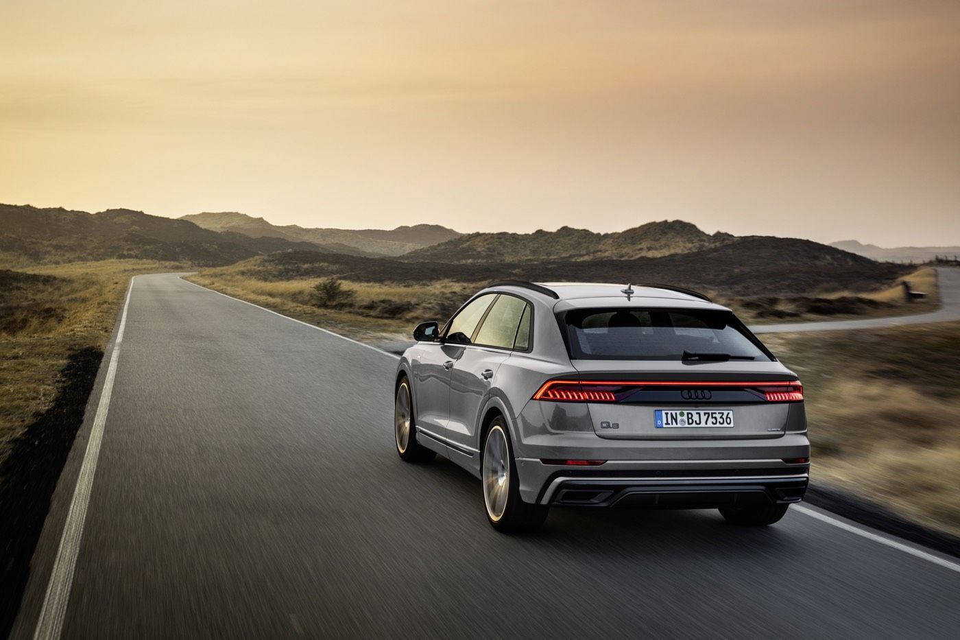Vue 3/4 arrière d'un VUS Audi Q8 gris roulant sur une route au bord de quelques collines