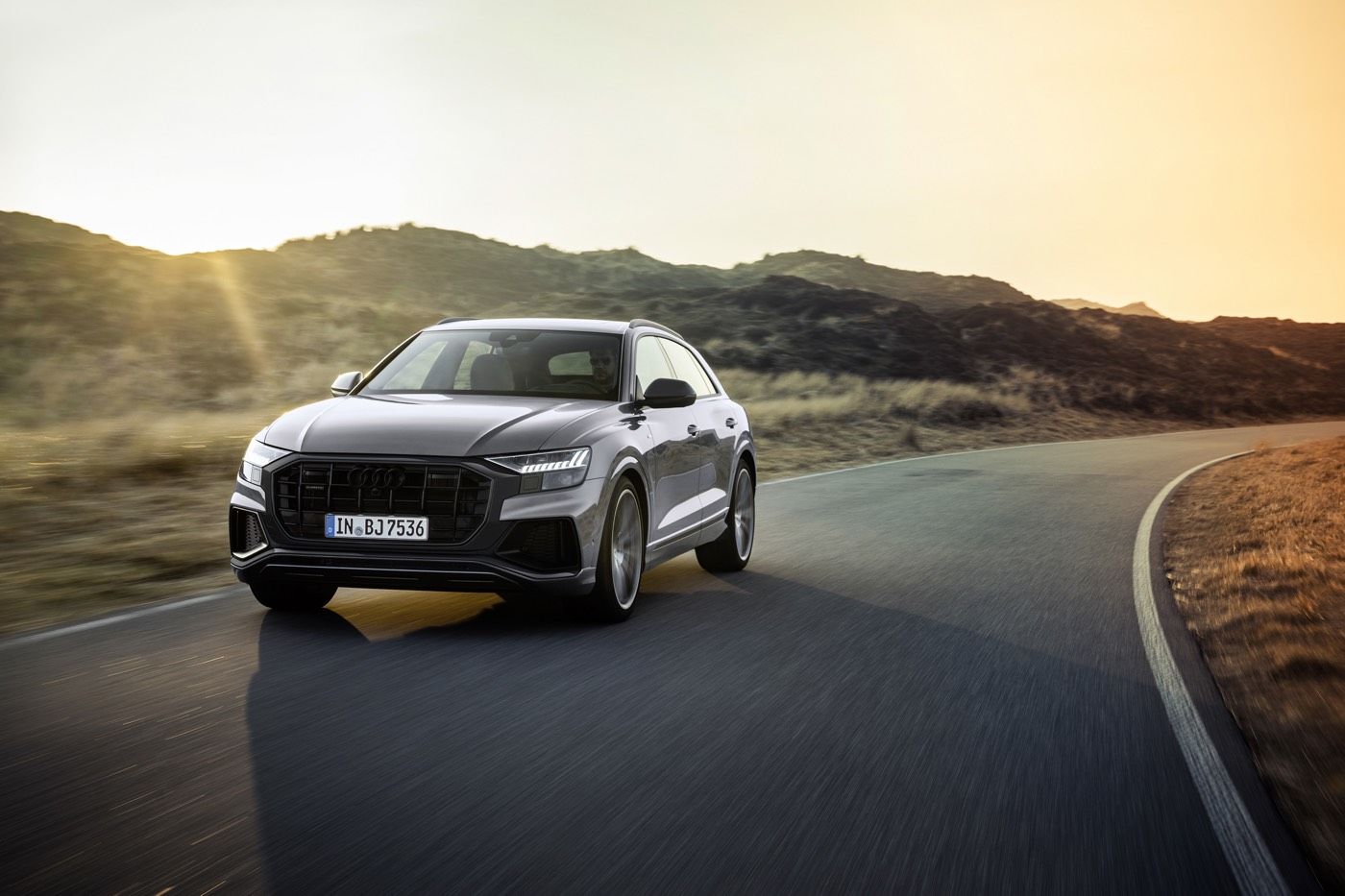 Vue 3/4 avant d'un VUS Audi Q8 gris roulant sur une route au bord de quelques collines