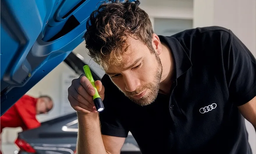 Audi technician inspecting the engine bay of a vehicle with the hood raised