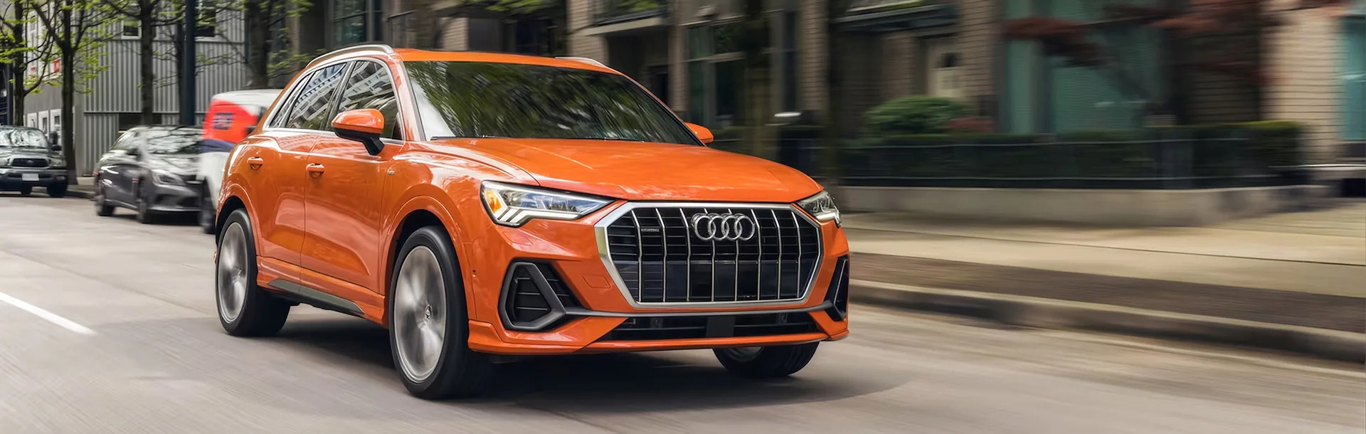 Orange Audi Q3 driving along a tree-lined city street