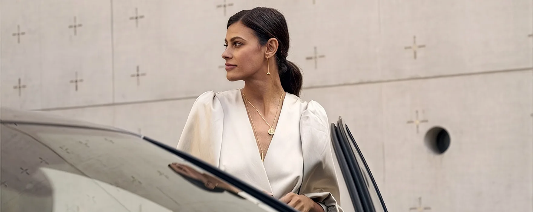 Woman in white stepping out of an Audi beside a concrete wall
