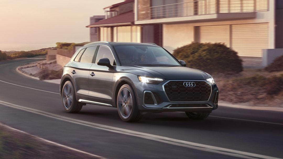 Vue 3/4 avant et latérale de l'Audi Q5 TFSI e hybride 2025, sur route en pleine puissance avec phares allumées