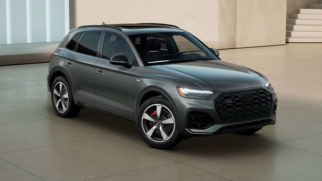 Vue 3/4 avant et latérale de l'Audi Q5 TFSI e hybride 2025, sortant du concessionnaire avec phares allumées