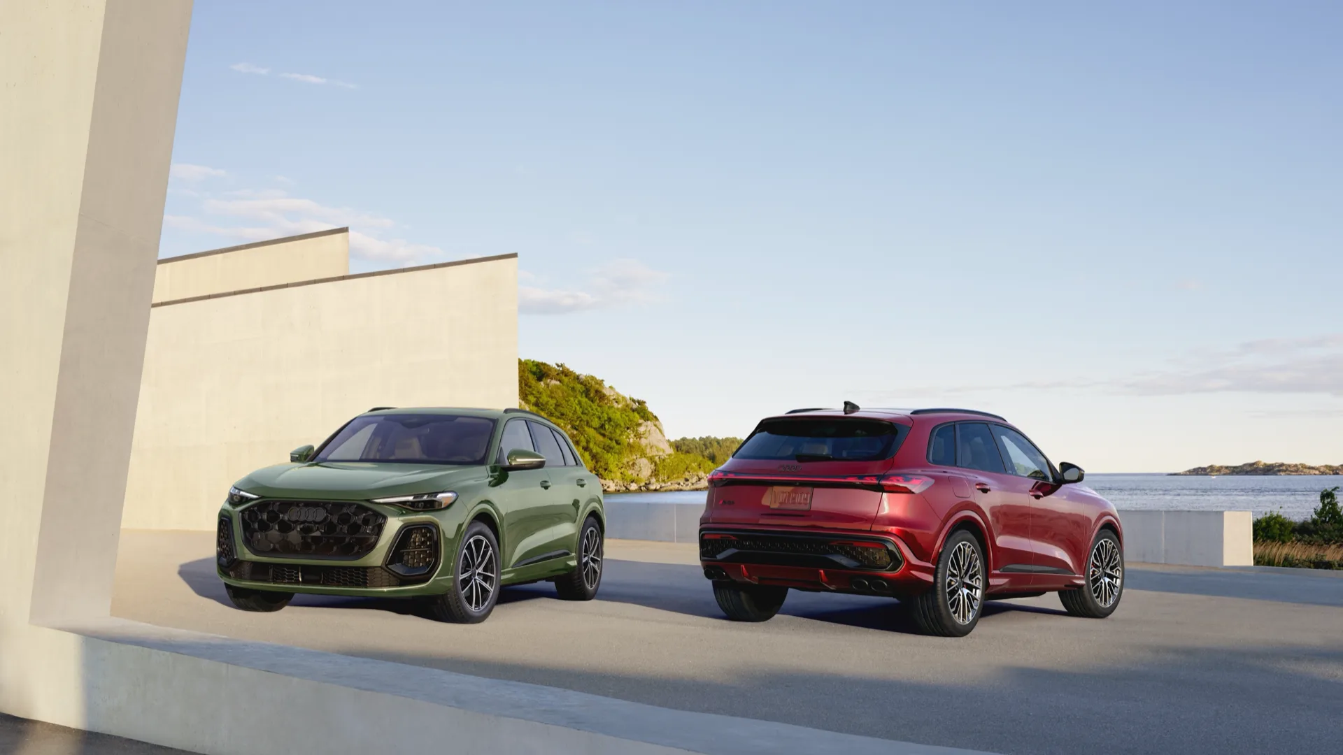 2026 Audi Q5 pair parked on a coastal terrace, green front three-quarter and red rear three-quarter