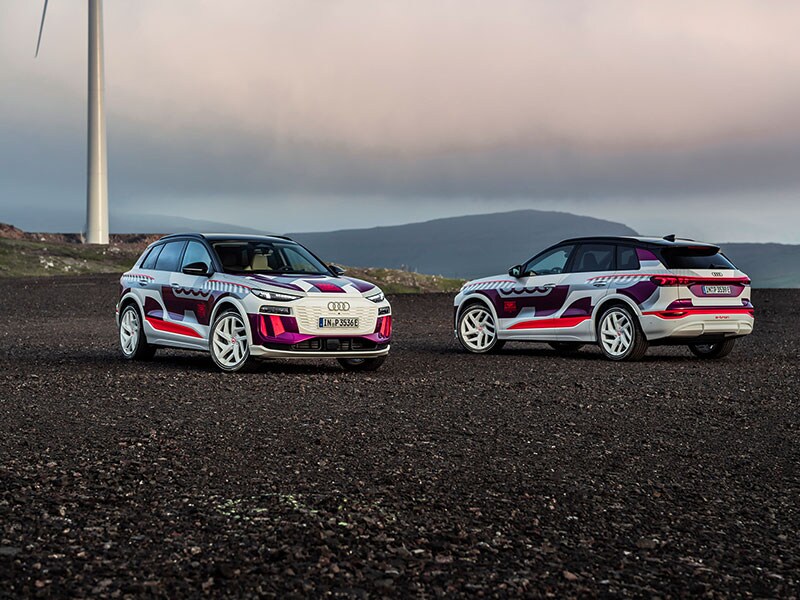 Two 2024 Audi Q6 e-trons on a mountain with windmill behind