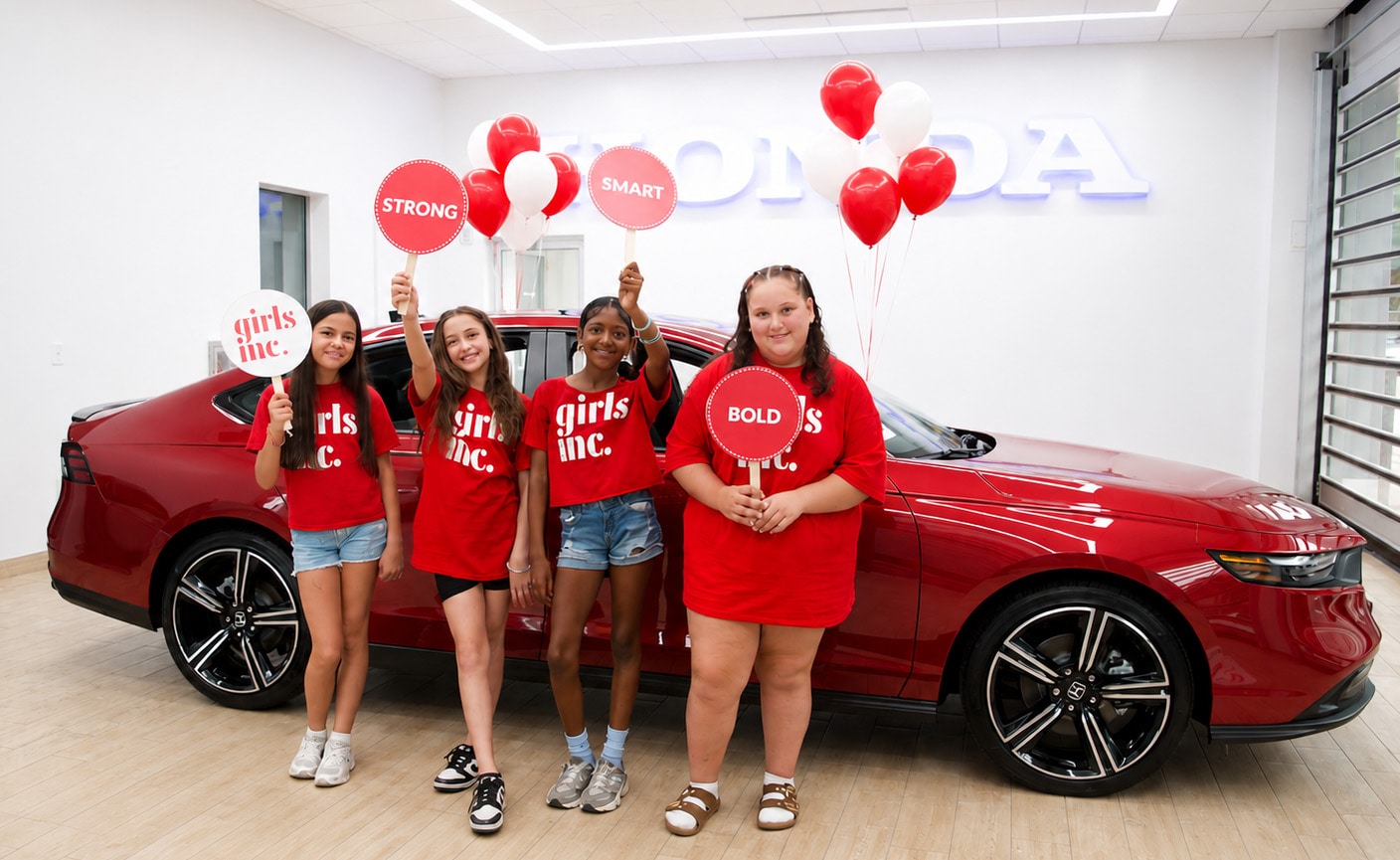 Girls Inc. members standing beside the Radiant Red Honda Accord Hybrid grand prize in the AutoFair Honda showroom