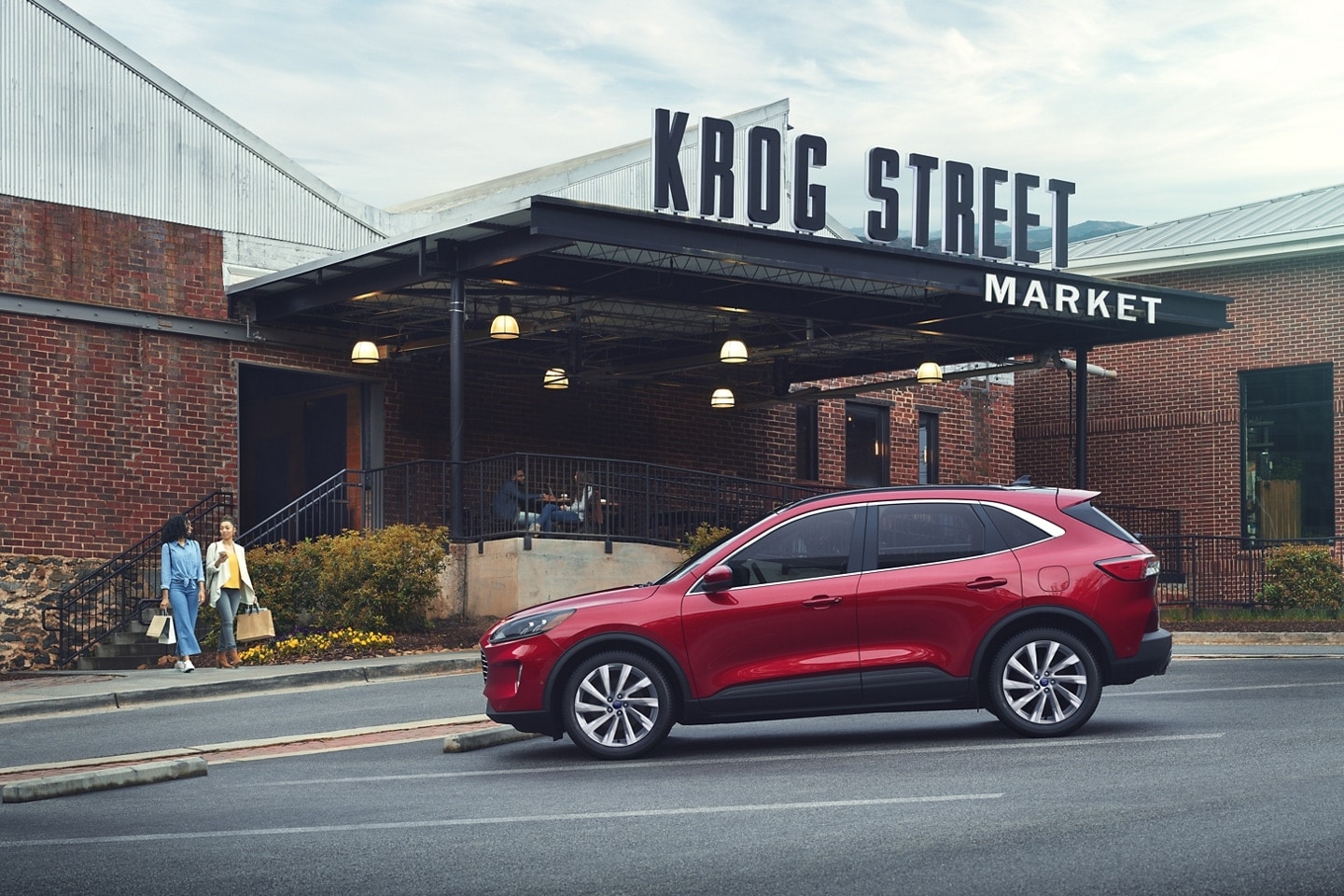 Two women walk toward a Red Ford Escape parked outside of a building with a sign that says KROG STREET MARKET