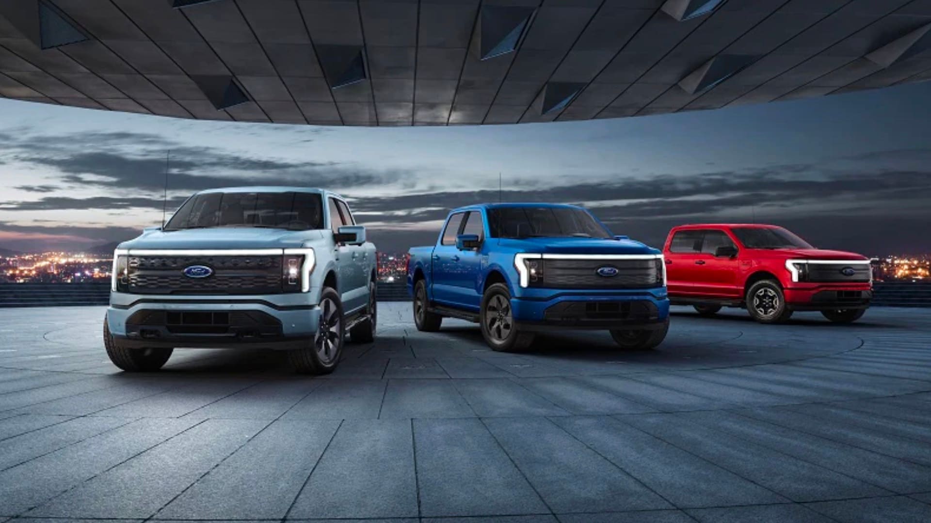 Fully Electric Ford F-150 Lightning Three Ford F-150 Lightning trucks facing the frame with a city skyline in the background