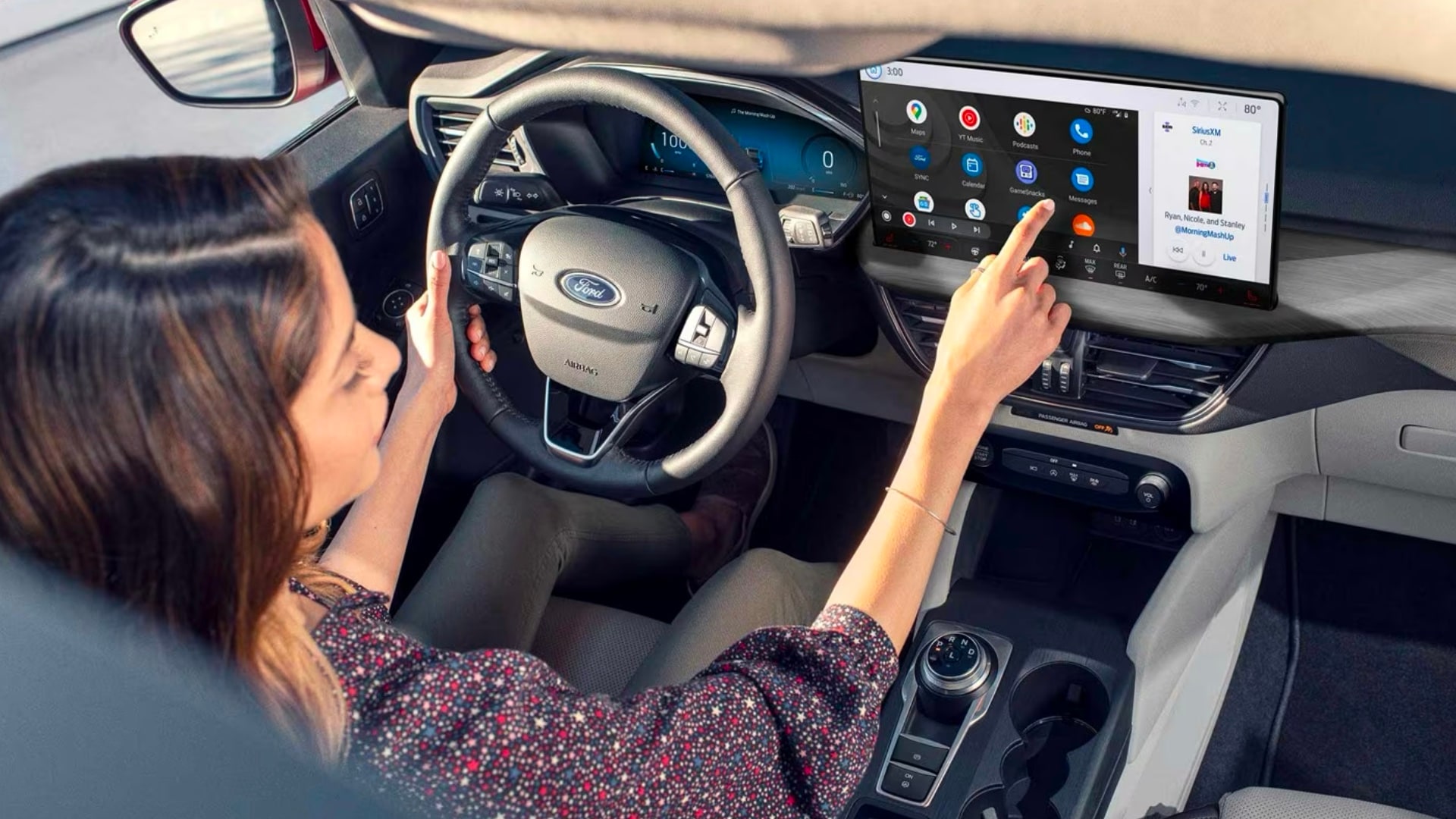 A woman sits in the driver's seat of a Ford using the touch screen displaying the Android Auto interface