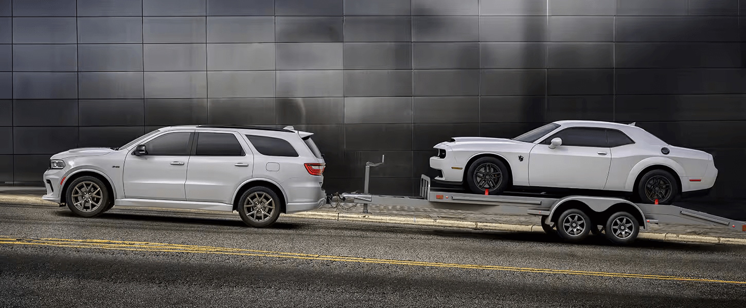Learn about the performance features of the Dodge Durango A white Dodge Durango towing a flat trailer with a Dodge muscle car on top
