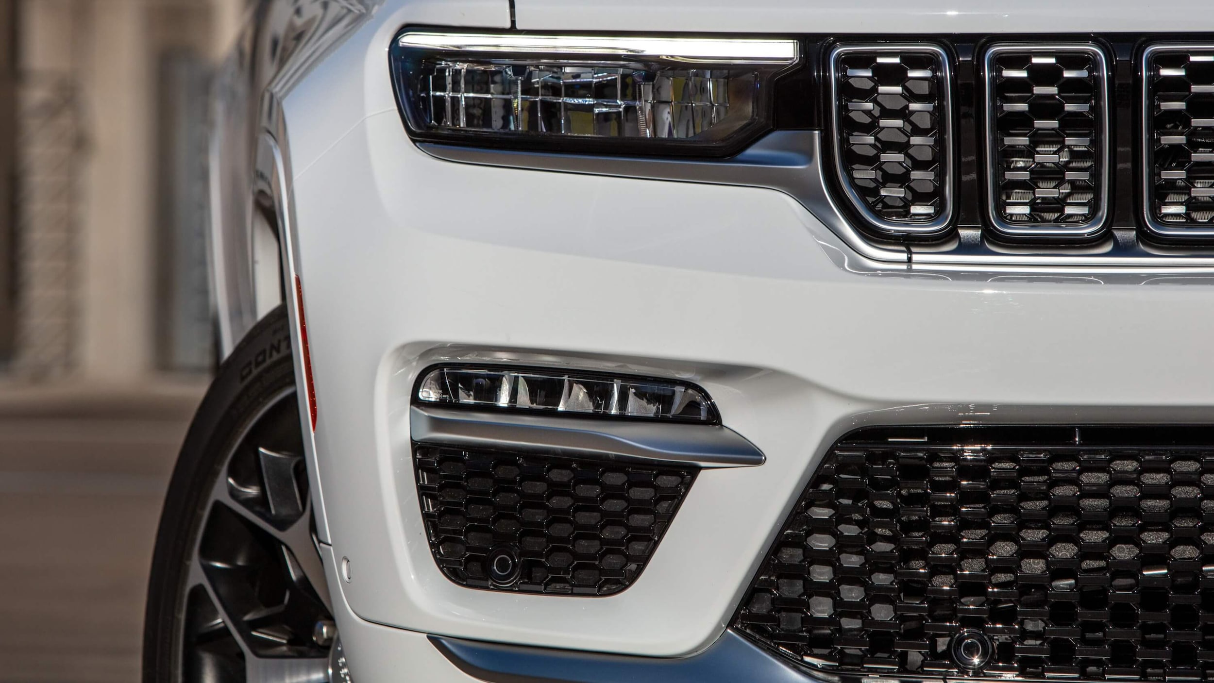 Learn about the exterior design of the Jeep Grand Cherokee 4xe Close up shot of the Jeep Grand Cherokee's front, showing the front grille, and right headlight