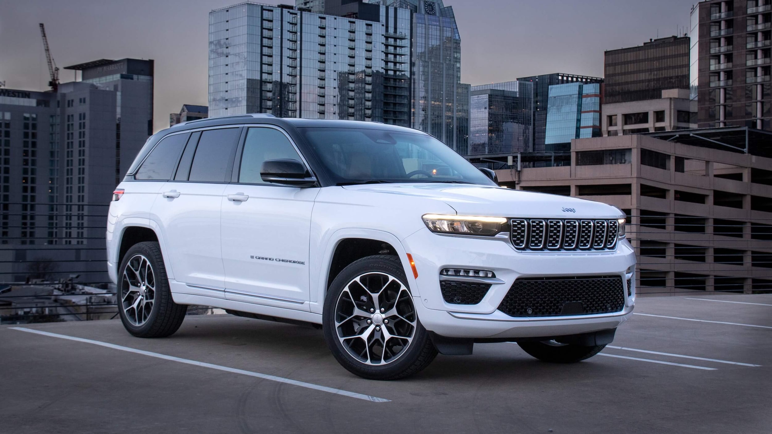 A white Jeep Grand Cherokee 4xe parked on the top floor of a parking garage in a city location
