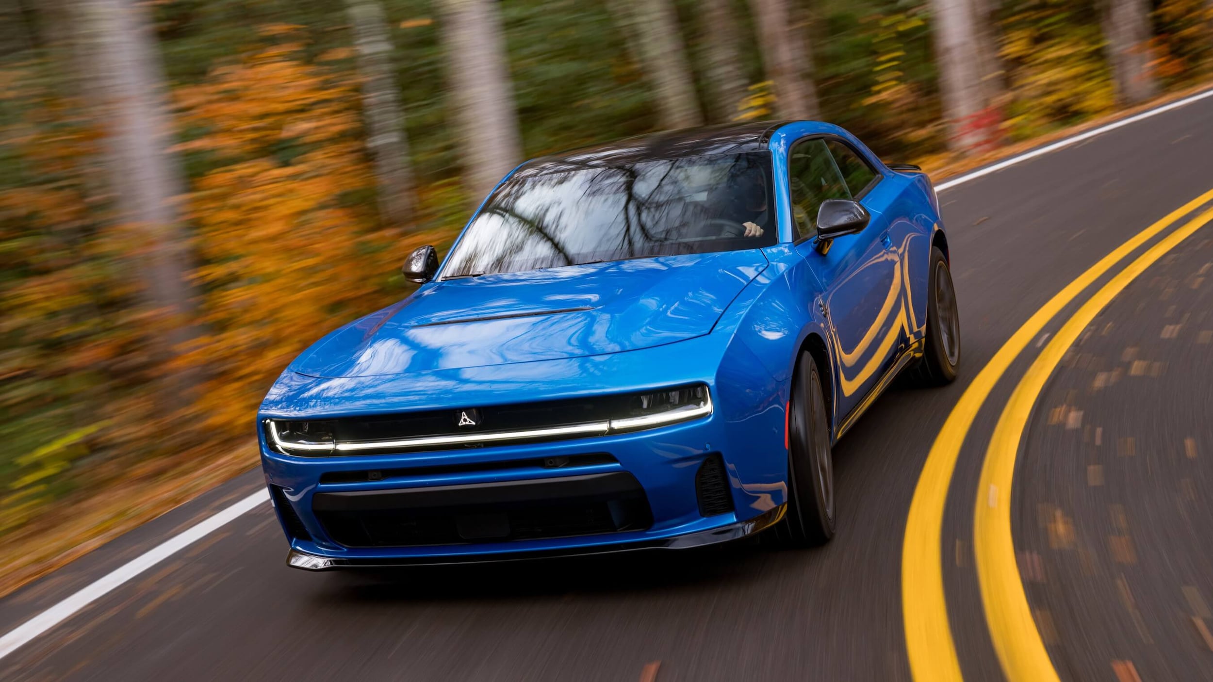 Blue Dodge Charger driving on a curved road through a forest