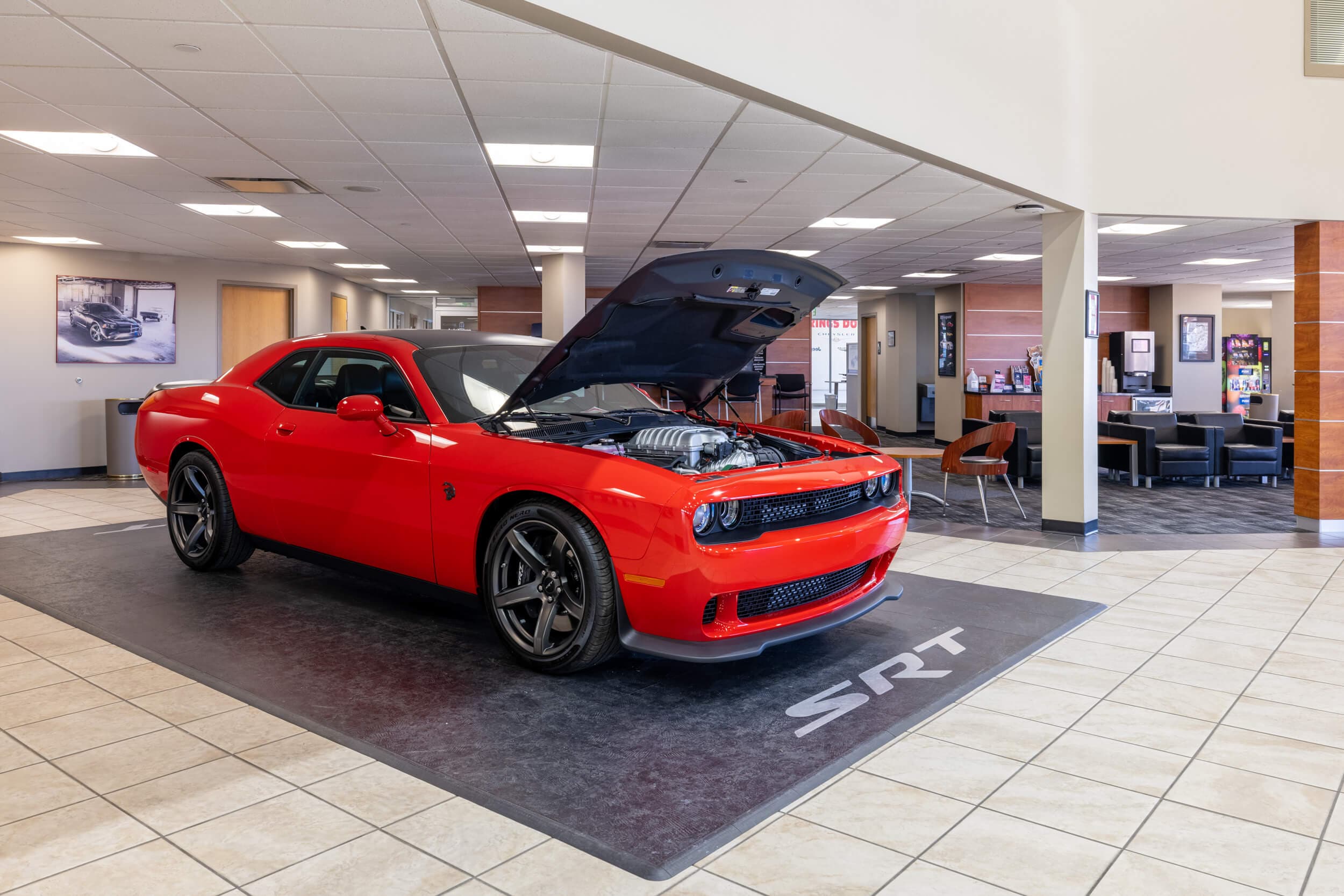 Interior of AutoNation Dodge Ram Colorado Springs in a space displaying a red Dodge SRT with its hood open, and some tables and chairs in the background