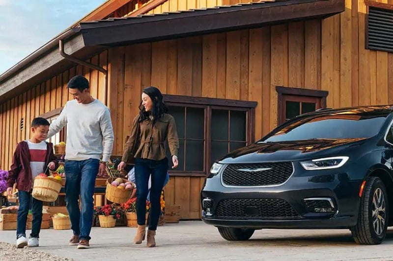 A family smiling in front of a Chrysler Pacifica