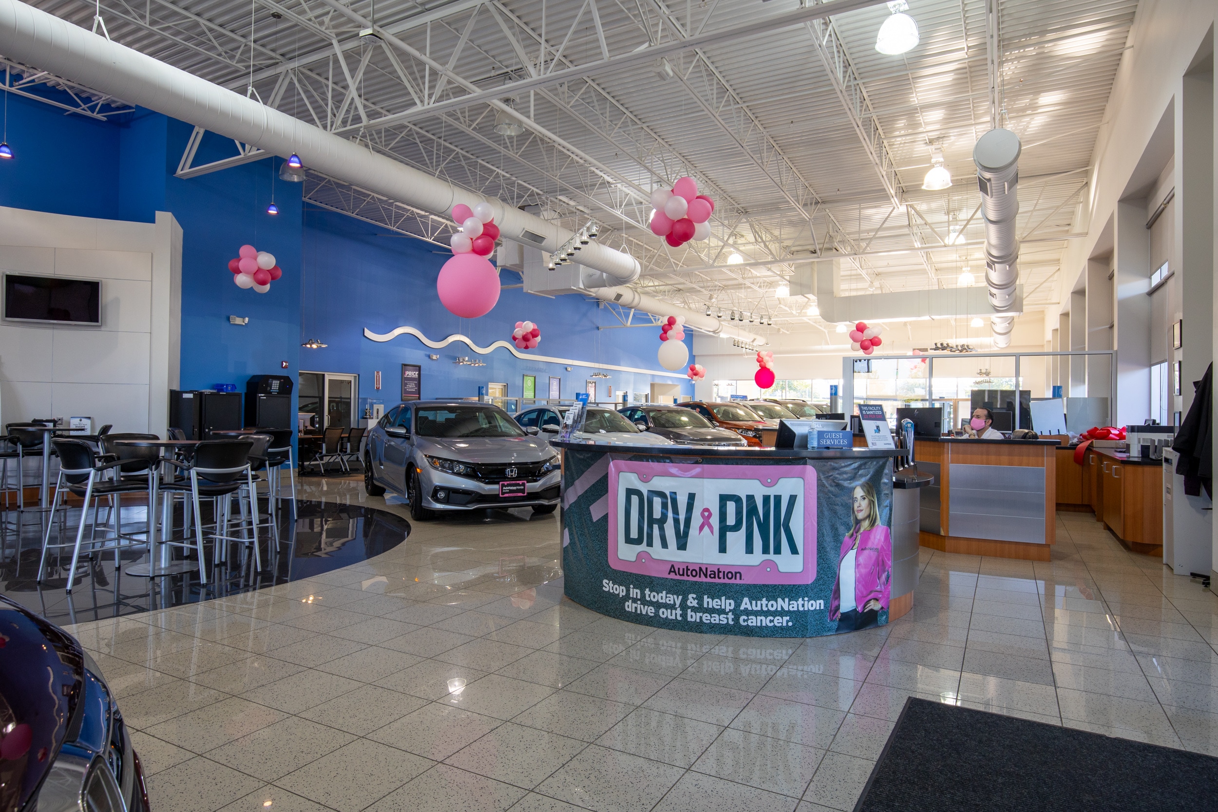 Interior view of AutoNation Honda Dulles with several vehicles parked inside along with multiple round tables and chairs.