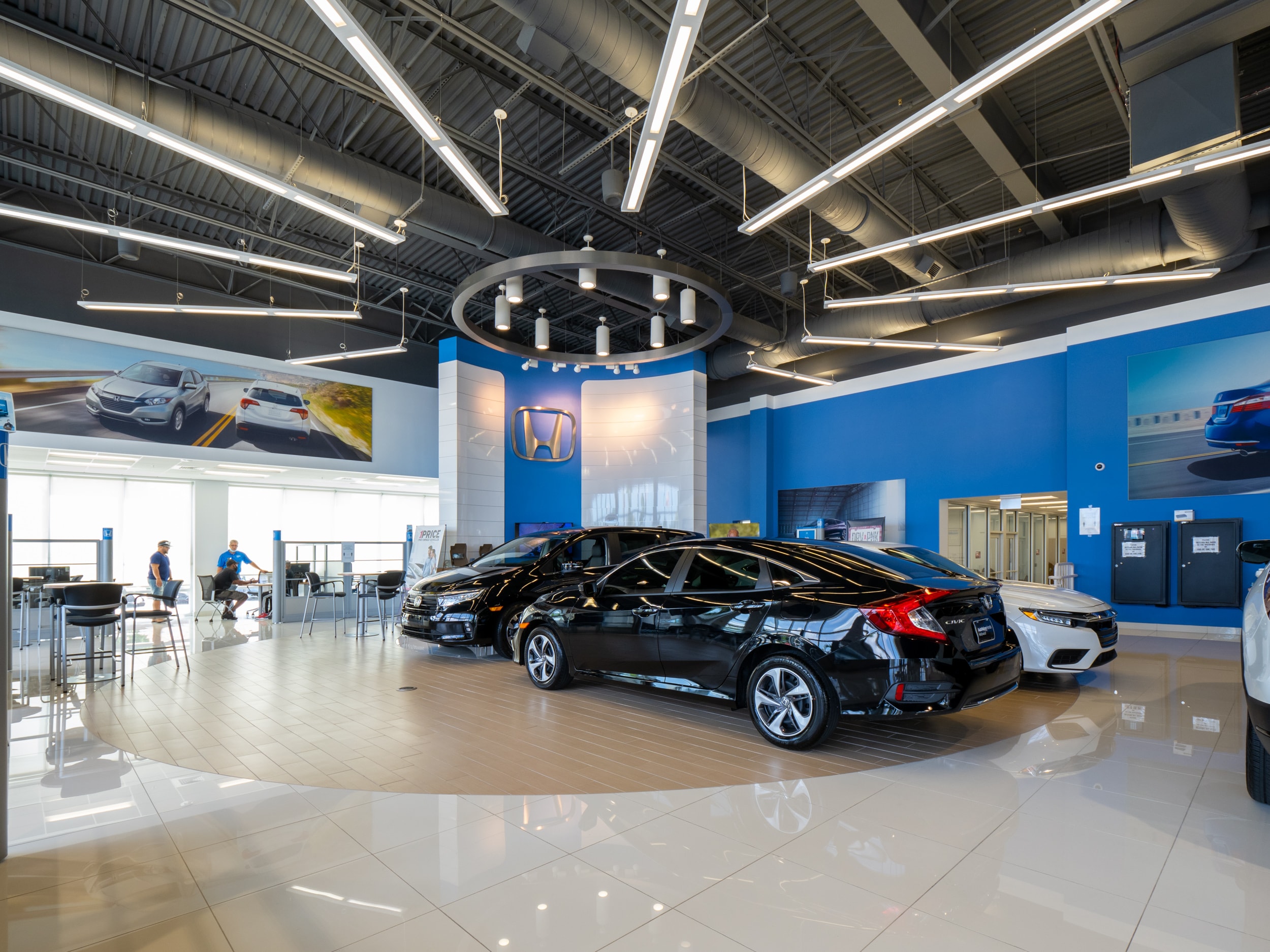 Interior view of AutoNation Honda Hollywood. Two black Hondas and several round tables with chairs.