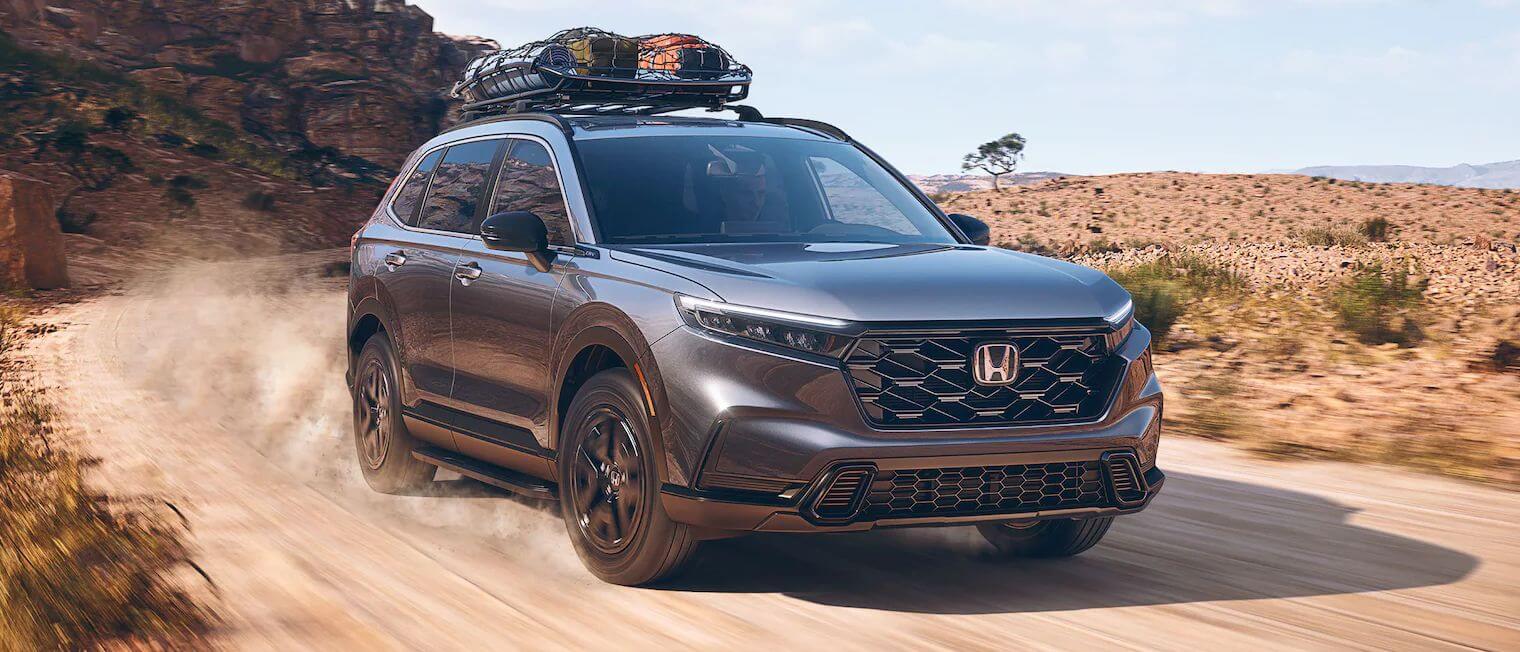 Honda CR-V Hybrid in Meteorite Gray Metallic Exterior shot of a Honda CR-V Hybrid in Meteorite Gray Metallic driving through a curved desert road.