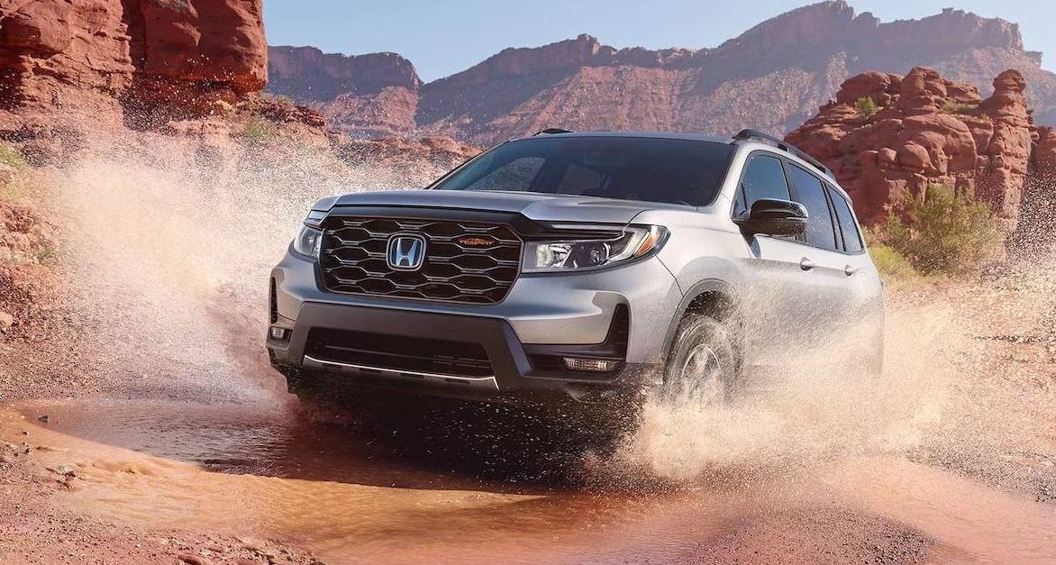 Honda Passport TrailSport in Lunar Silver Metallic Honda Passport TrailSport in Lunar Silver Metallic driving through a puddle in a rocky desert surrounding.