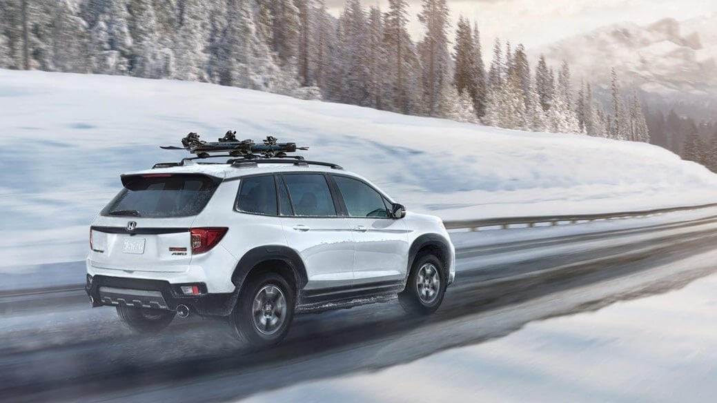 Learn which Honda models can have all-wheel drive, like the Honda Passport Exterior shot of the Honda Passport TrailSport in Platinum White Pearl, driving through a snow and ice covered road.