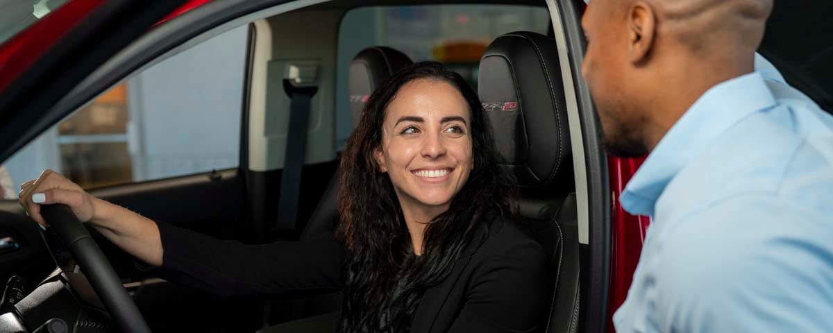 Image of a woman smiling while in the front seat of a red vehicle