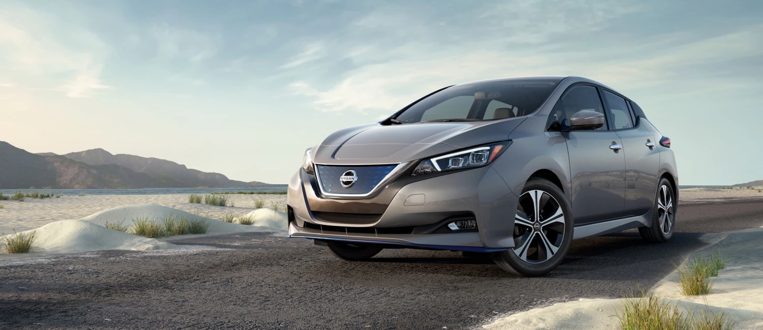 Grey Nissan Leaf in the desert near mountains on a partially cloudy day.
