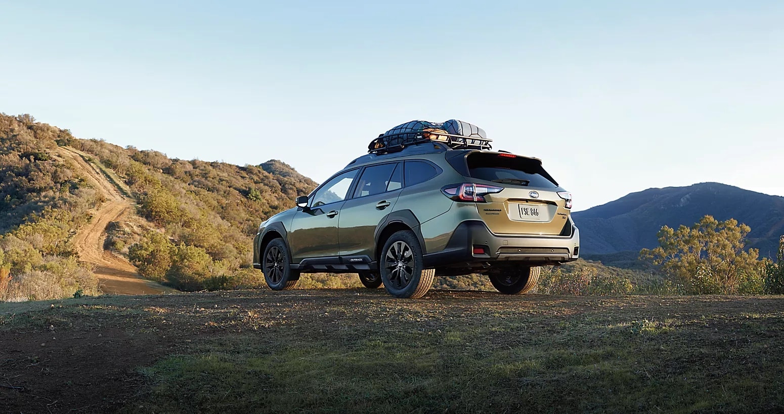 A Subaru Outback sits in a mountainous natural area with camping gear strapped onto on the roof rack.