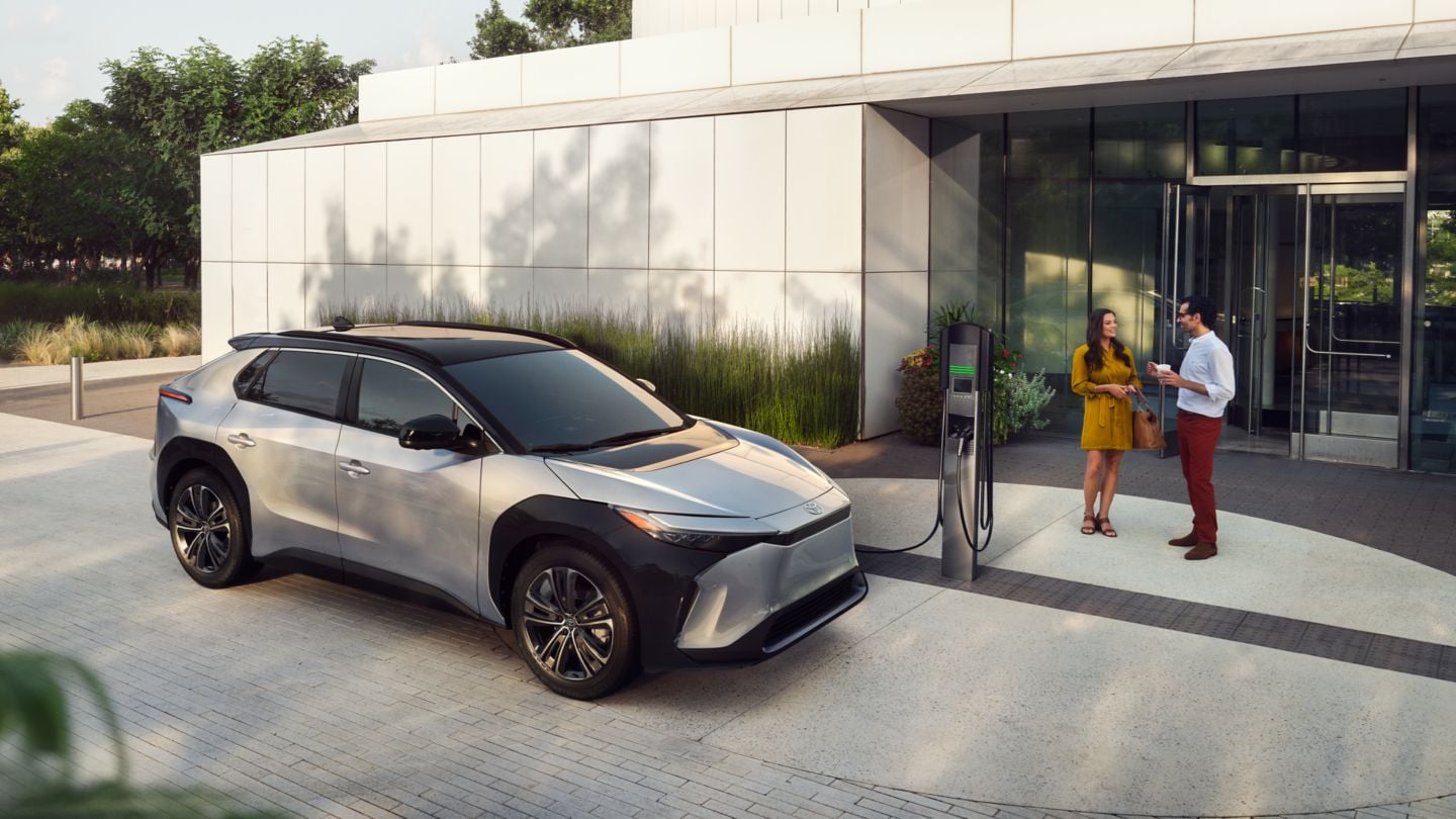 Silver Toyota bZ4X charging at a charging station in front of a white building