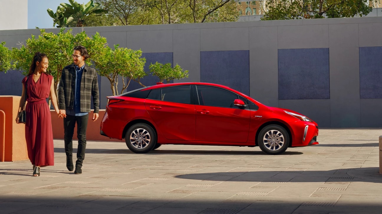 Red Toyota Prius parked in the driveway of a modern home with a couple walking away from the vehicle