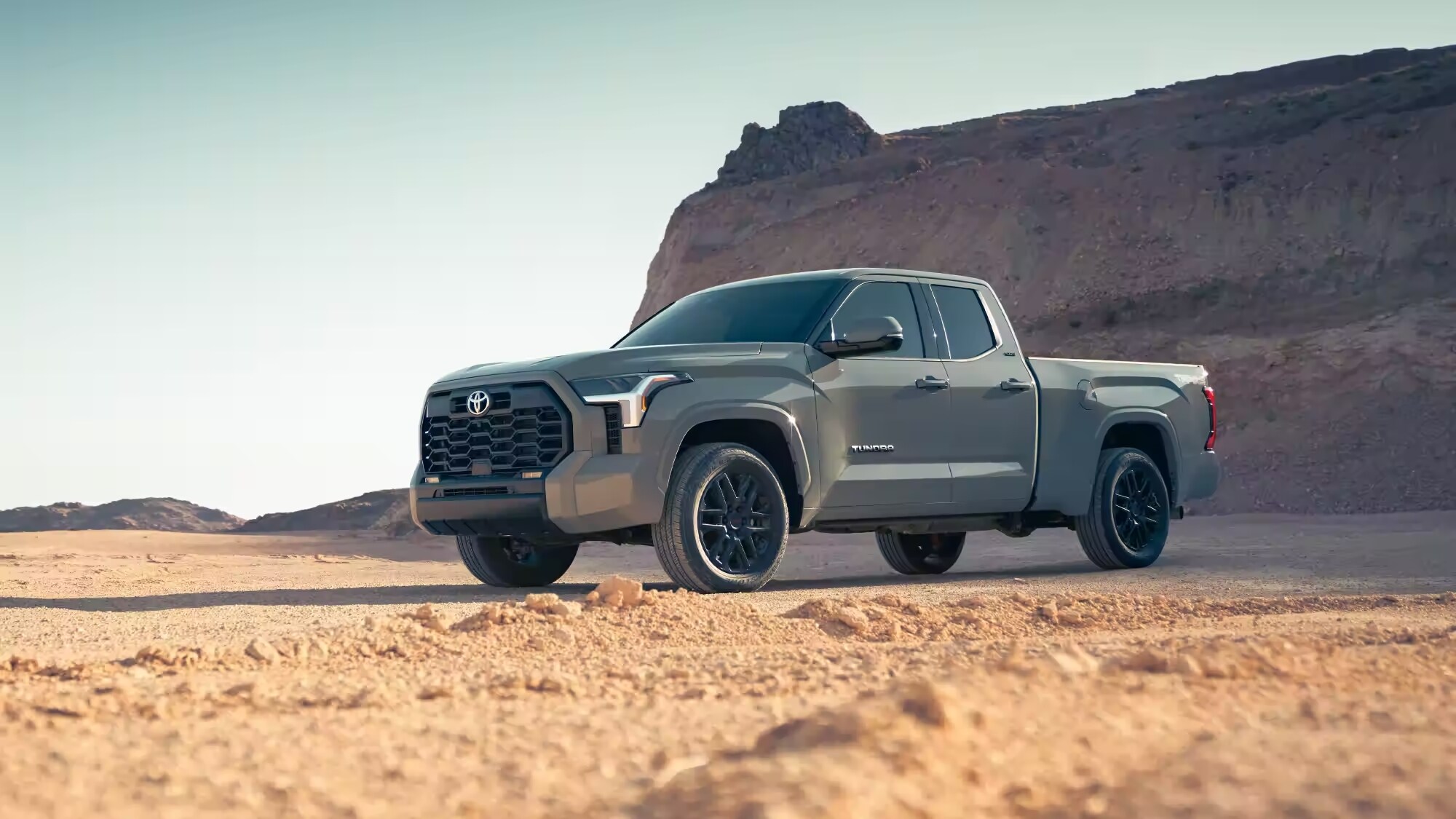 Silver Toyota Tundra parked in the desert with a mountain face in the background