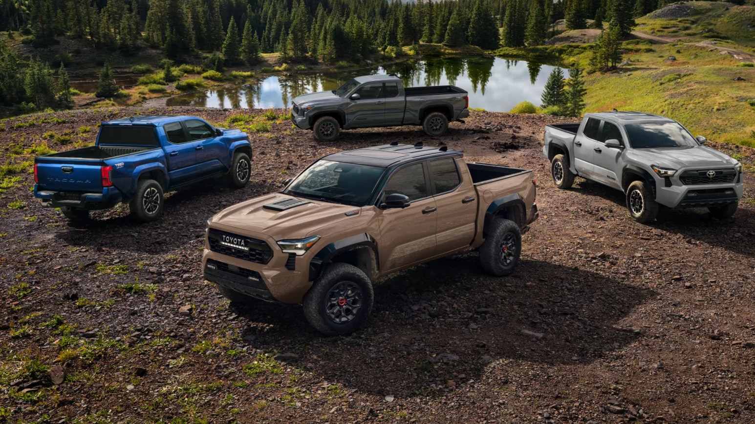 Four Toyota Tacoma trucks parked overlooking a body of water in the mountains