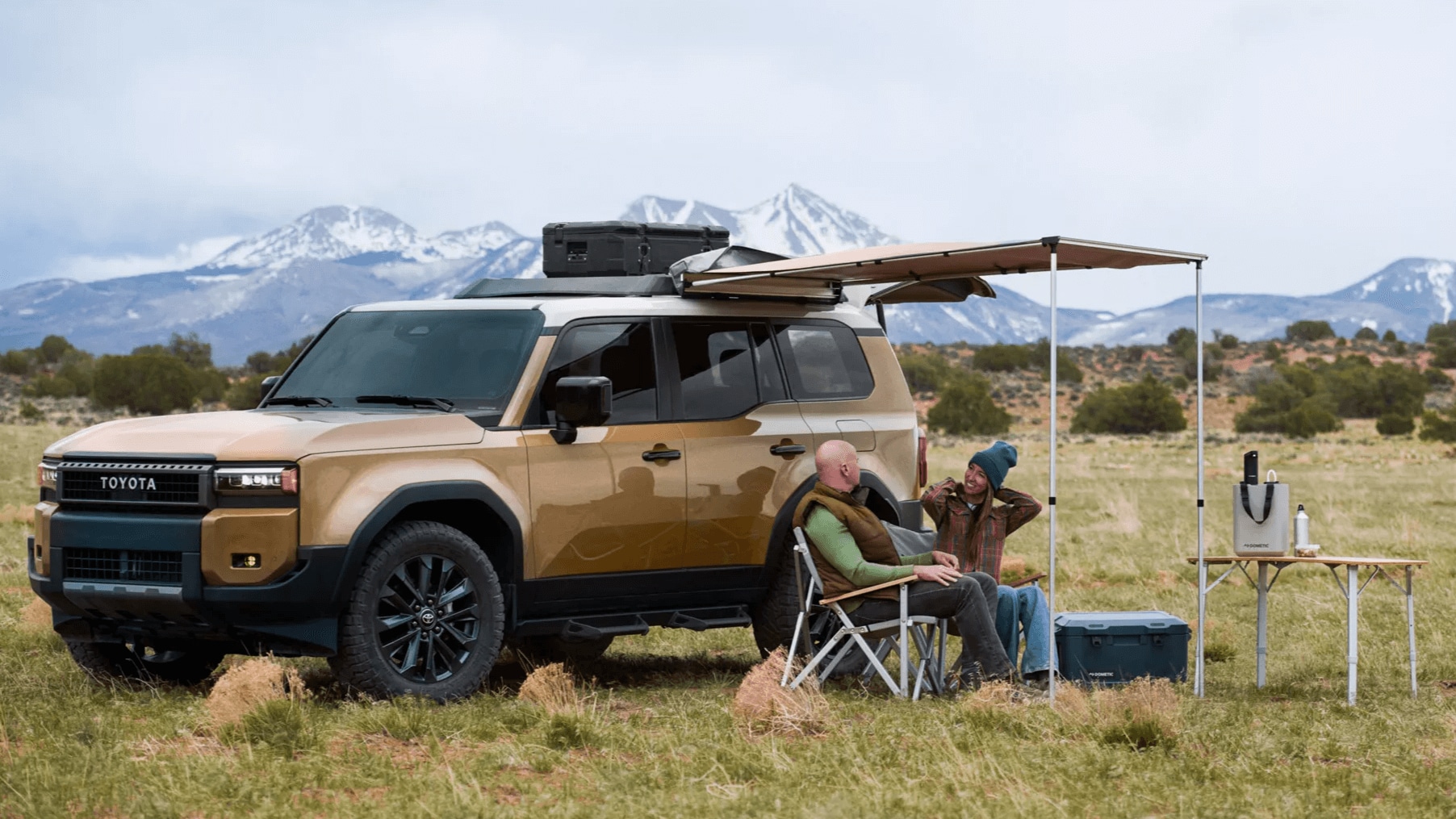 Outdoor shot of a Toyota Land Cruiser used as a campsite with two adults sitting under canopy that's attached to the side of the Land Cruiser