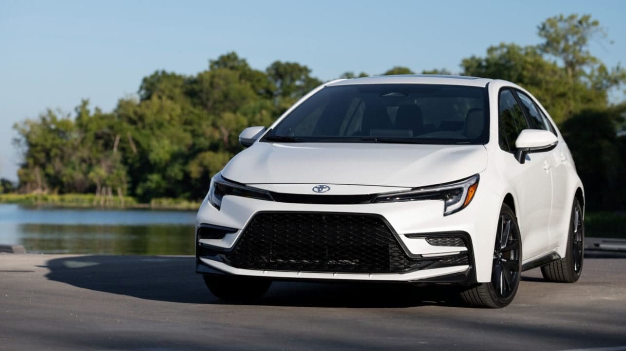A white Toyota Corolla sitting parked in front of a pond