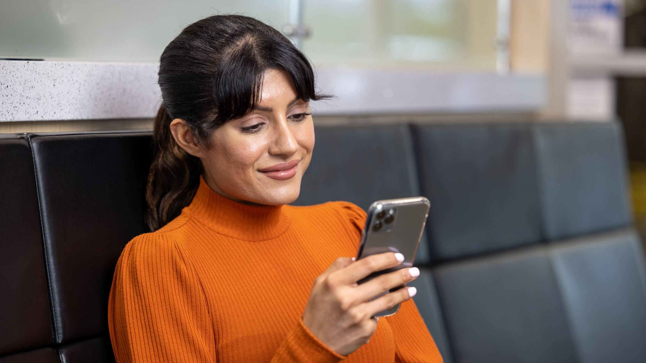 Woman in an orange sweater looking at her cell phone