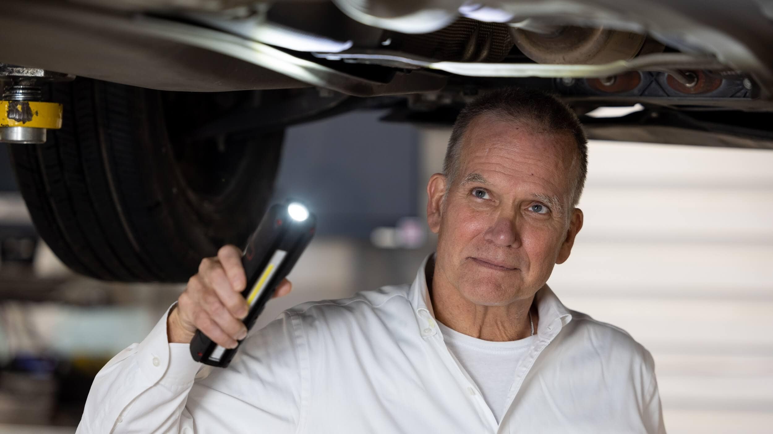 A service technician shining a flashlight on the underside of a vehicle
