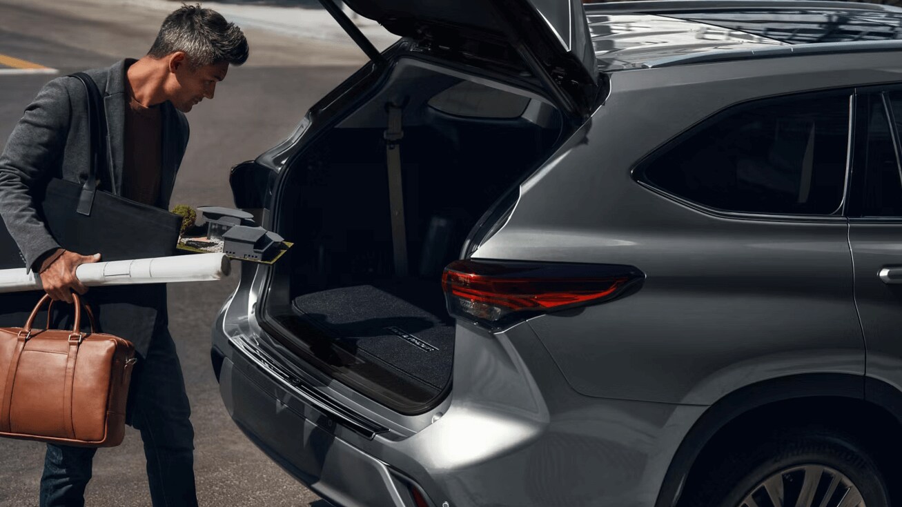 Highlander (3).png A man putting bags and project materils in the back of a Toyota Highlander with the liftgate opened.