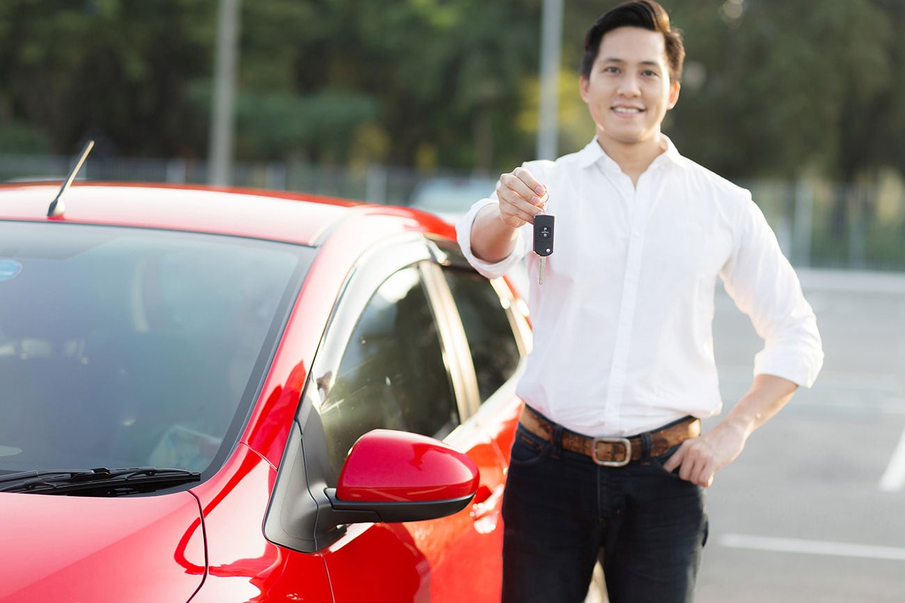 A Man Holding Up Car Keys Next to a Red Car