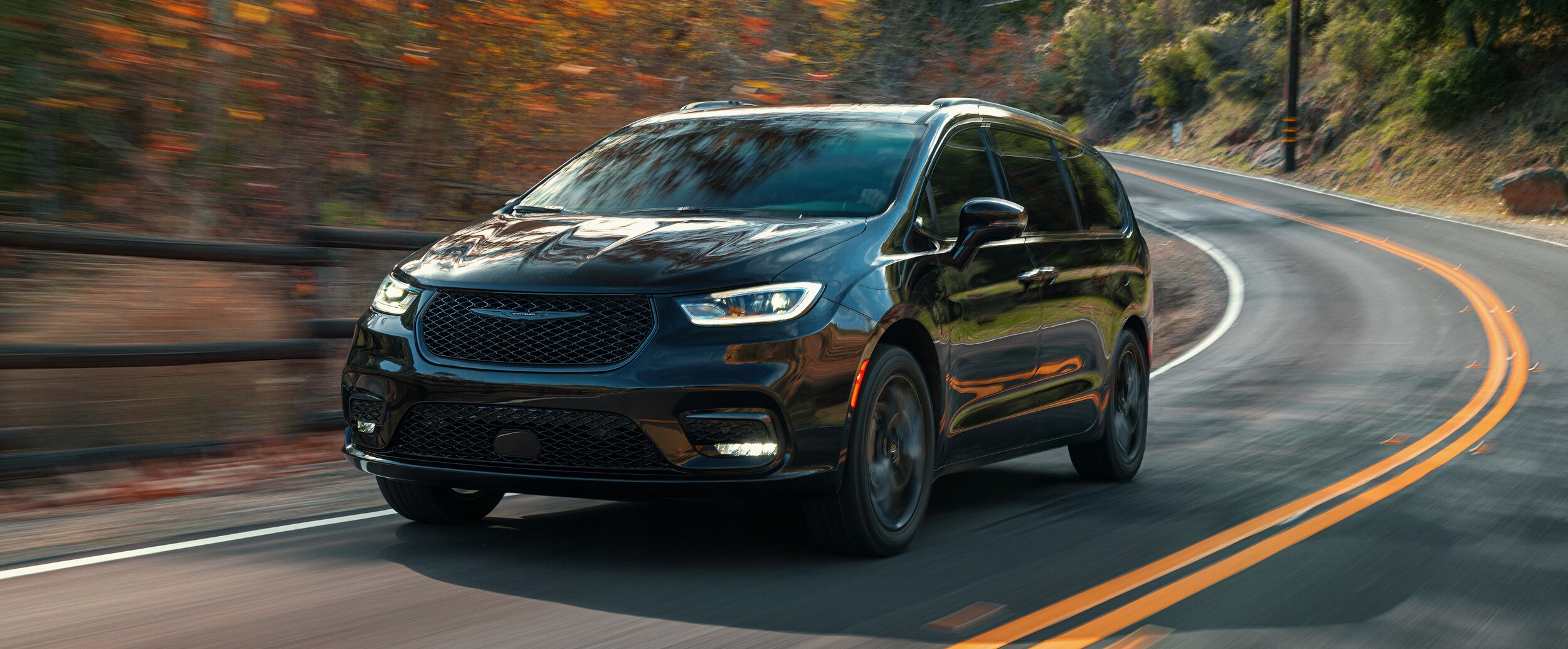 2021 Chrysler Pacifica driving on a road in front of red and gold fall trees; Chrysler Pacifica is available at our RI Dealership