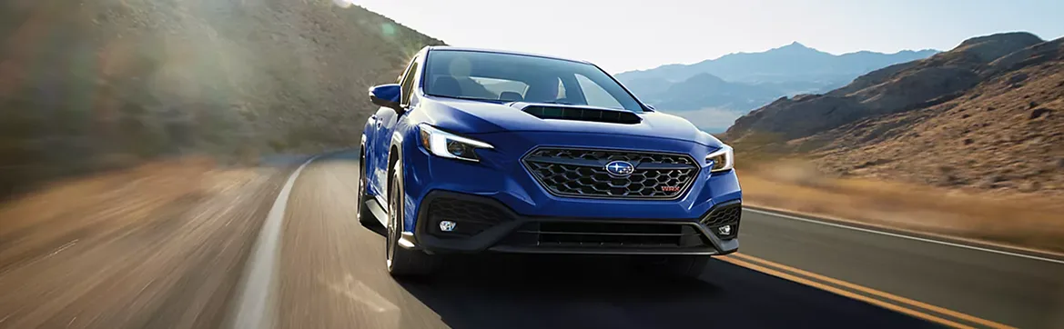 A blue Subaru WRX accelerating along a coastal road