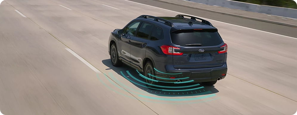 A dark Subaru SUV on a highway with teal blind-spot detection waves shown along its rear quarter